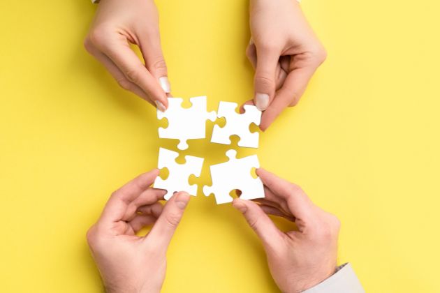 quatre mains tenant chacune une pièce de puzzle blanche pouvant s’emboîter les unes dans les autres
